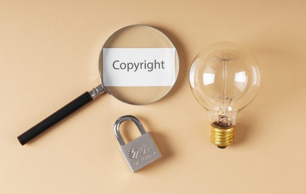 Lente d'ingrandimento su un foglio con la scritta "Copyright", accanto a un lucchetto e una lampadina, simboli della proprietà intellettuale.